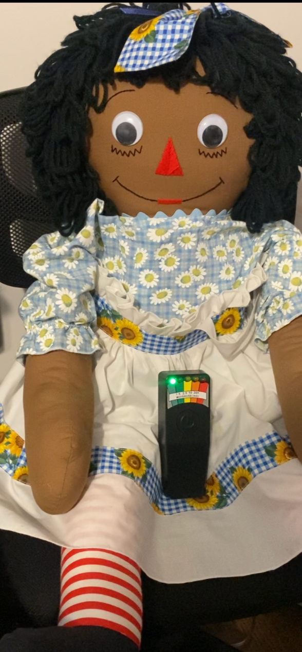 Haunted Raggedy Ann doll with a floral dress and striped socks sitting on a chair.