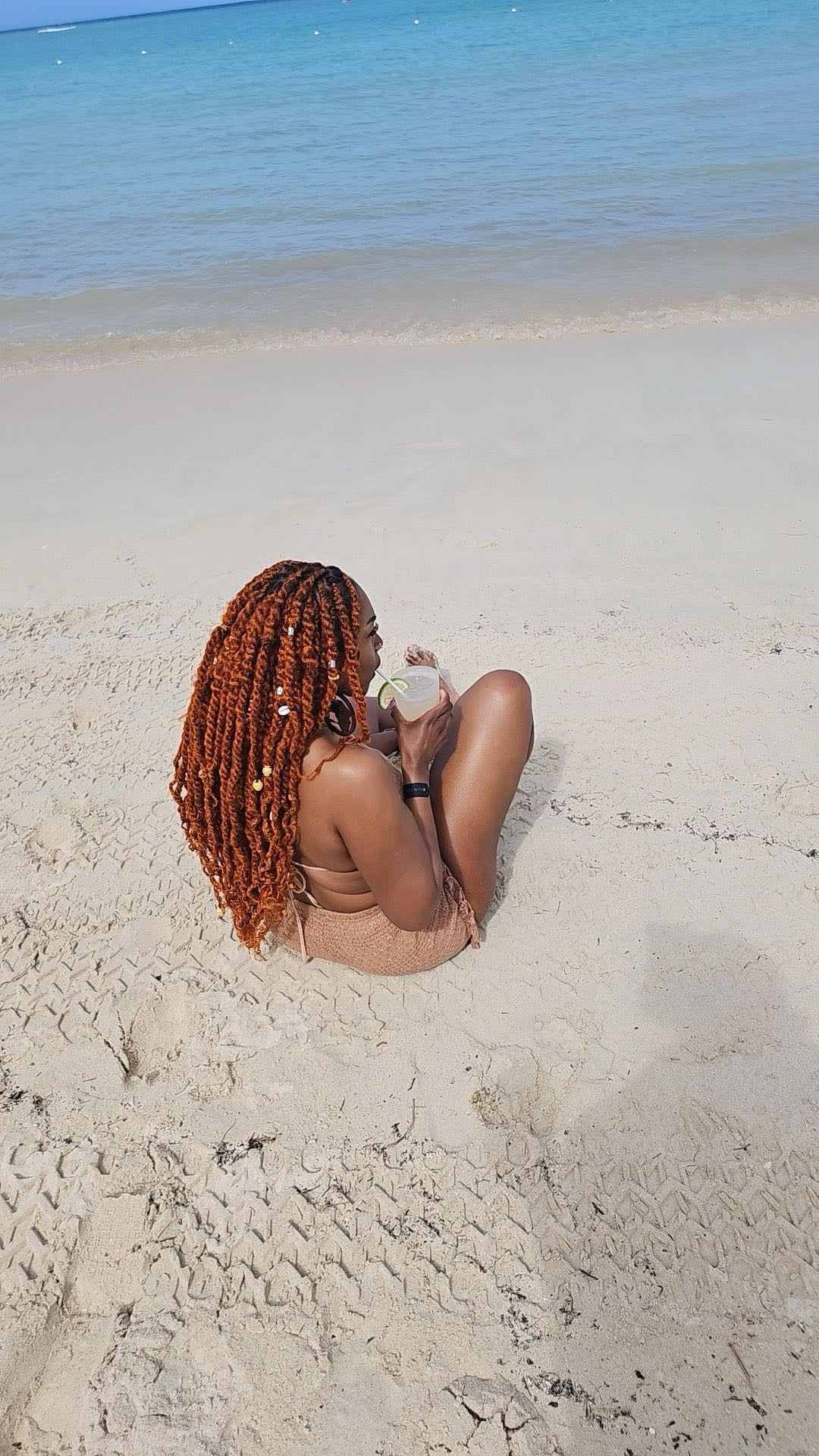 Owner with braided hair sitting on a sandy beach with clear blue water