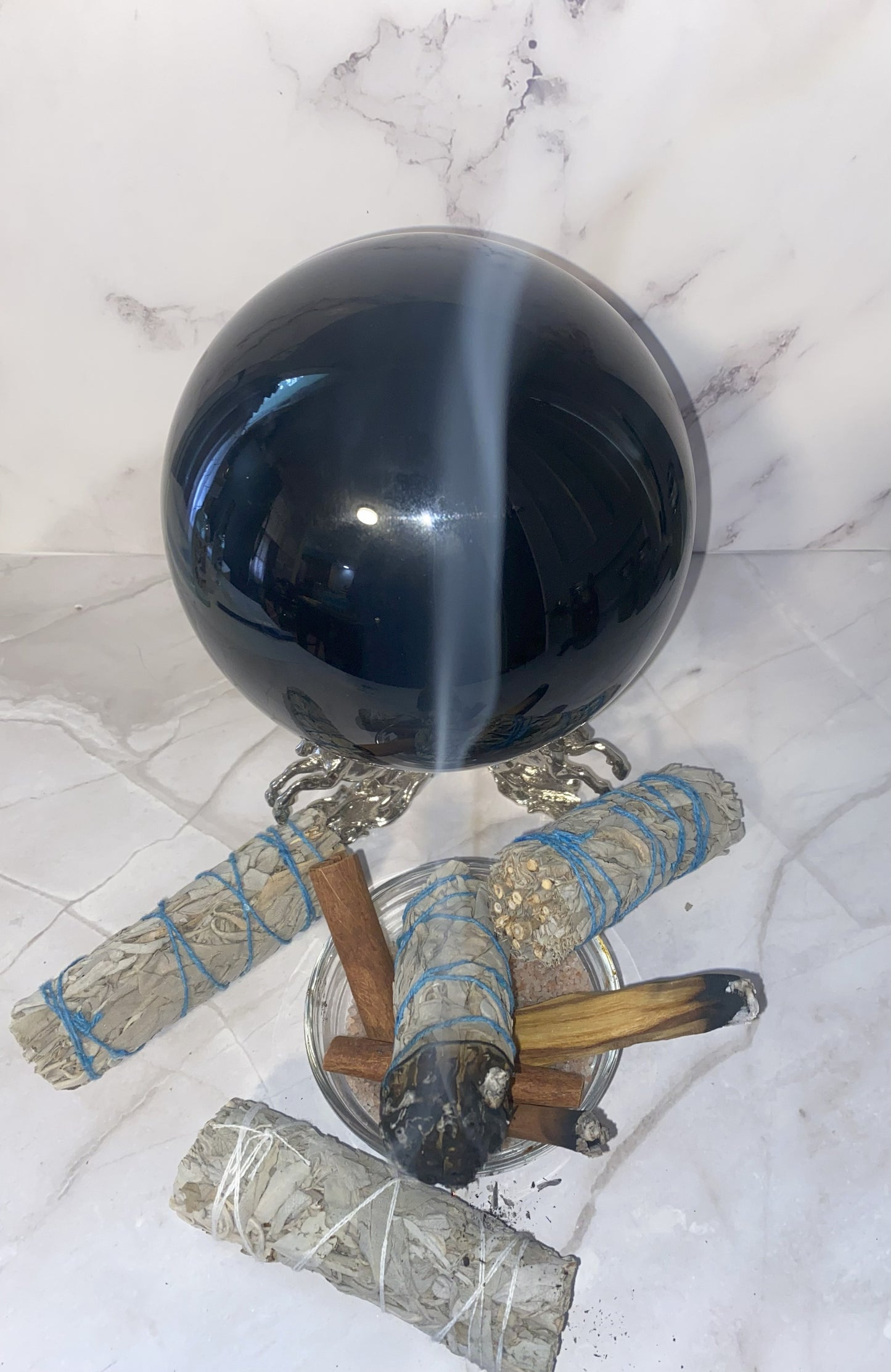 Black crystal ball with smoldering sage on a marble surface